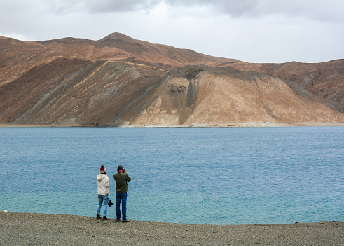 Ladakh, India - Jul 20, 2015. A couple standing and looking at Pangong Lake in Leh, Ladakh, India. Pangong Tso Tibetan for high grassland lake, is an endorheic lake in the Himalayas situated at a height of about 4,350 m.