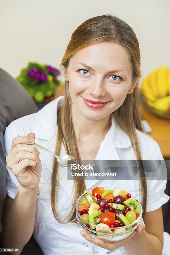 Jovem mulher olhando para a câmera, sorrindo, segurando salada de frutas fresca. - Foto de stock de 30 Anos royalty-free