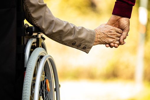Elderly people in wheelchair holding hands together.
