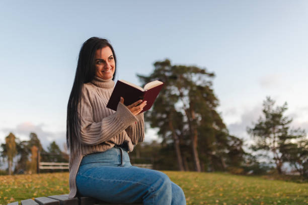 istock Beautiful young woman sitting on a park bench and reading a book 1748290099