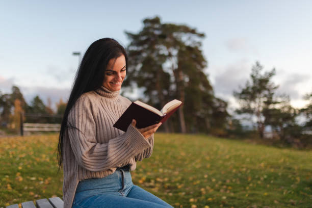 istock Beautiful young woman sitting on a park bench and reading a book 1748290100