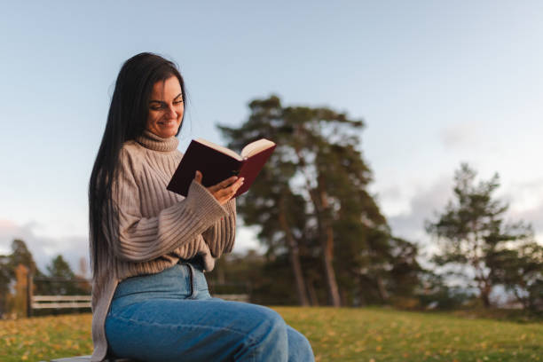 istock Beautiful young woman sitting on a park bench and reading a book 1748290103