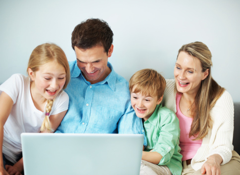 A pair of young parents and their two children using their laptop together at home