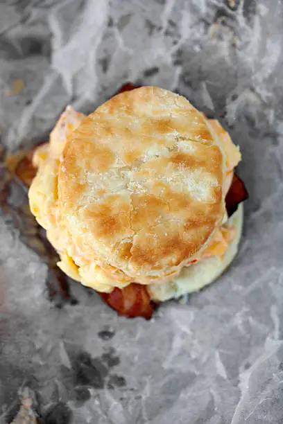 "A homemade, southern biscuit with scrambled eggs, cheese, and bacon on crumpled wax paper.View more of my"