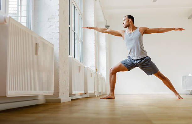 Young black man practicing Yoga. Young black man practicing the Warrior yoga pose. Horizontal shot. warrior position stock pictures, royalty-free photos & images