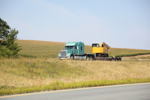 Semi truck hauling a flat bed trailer with a new excavator. Selective focus on truck and trailer.For similar pictures go to