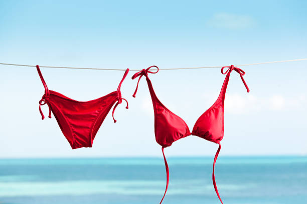 Tropical Beach Vacation with Bikini Swimwear Drying on Clothes Line Subject: Bikini swimwear hanging on clothesline for drying, vacationing on tropical beach holiday. bathing suit stock pictures, royalty-free photos & images