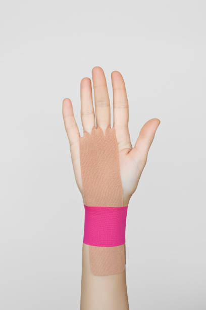 ベージュとピンクのキネシオテープによる女性の手の手首関節の固定 - sprain human joint palm human arm ストックフォトと画像