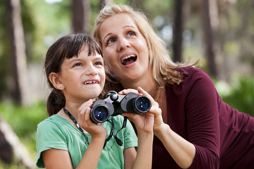 Hispanic mother (30s) and daughter (7 years) in the woods, with pair of binoculars.   Focus on little girl.