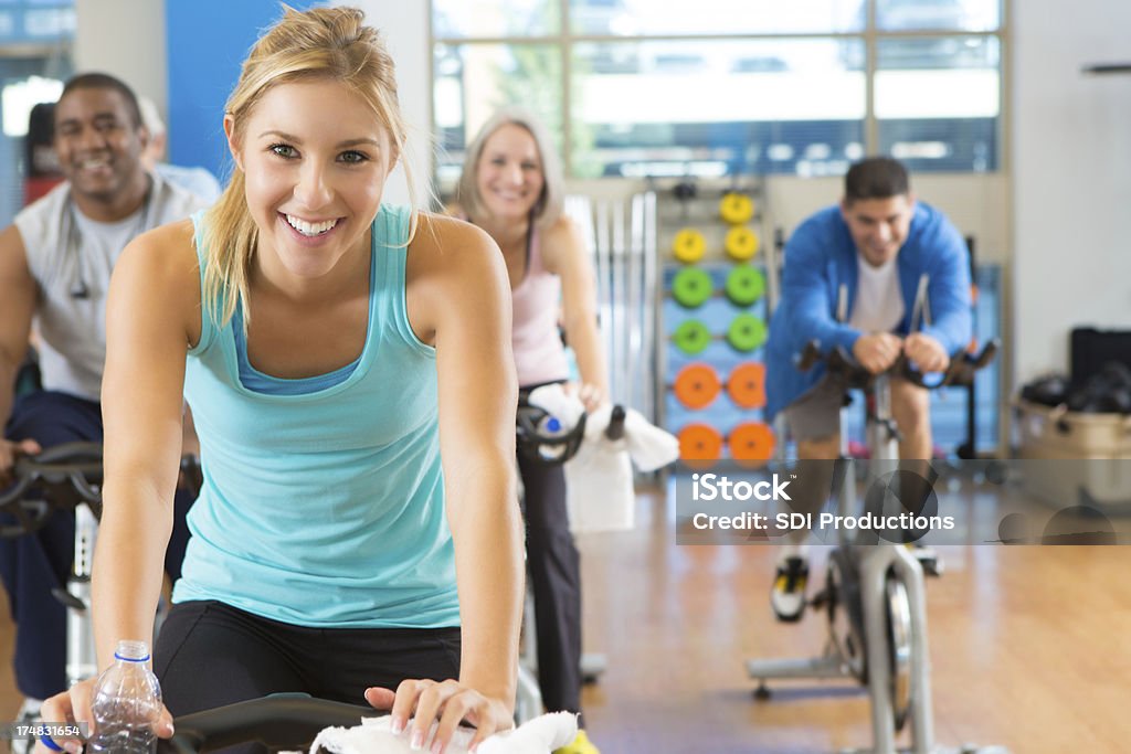 Sorrindo homens e mulheres em bicicletas ergométricas uma academia de ginástica - Foto de stock de Academia de ginástica royalty-free