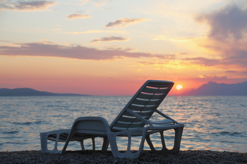 empty single white plastic sunbed against mediterranean ocean sunset