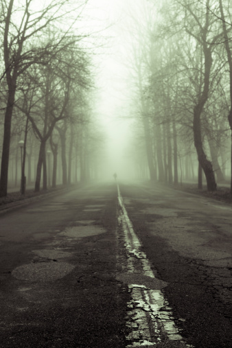 Human sihouette coming from the fog in an old road