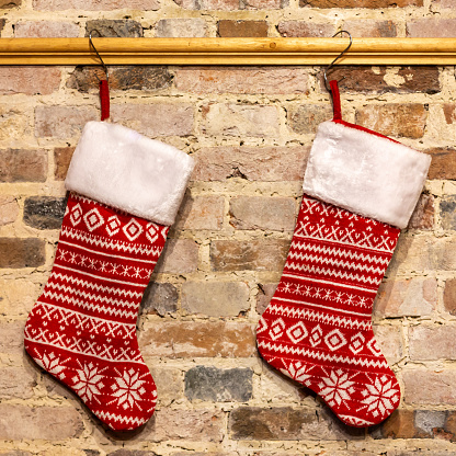 Two Christmas stockings hanging up against a brick wall