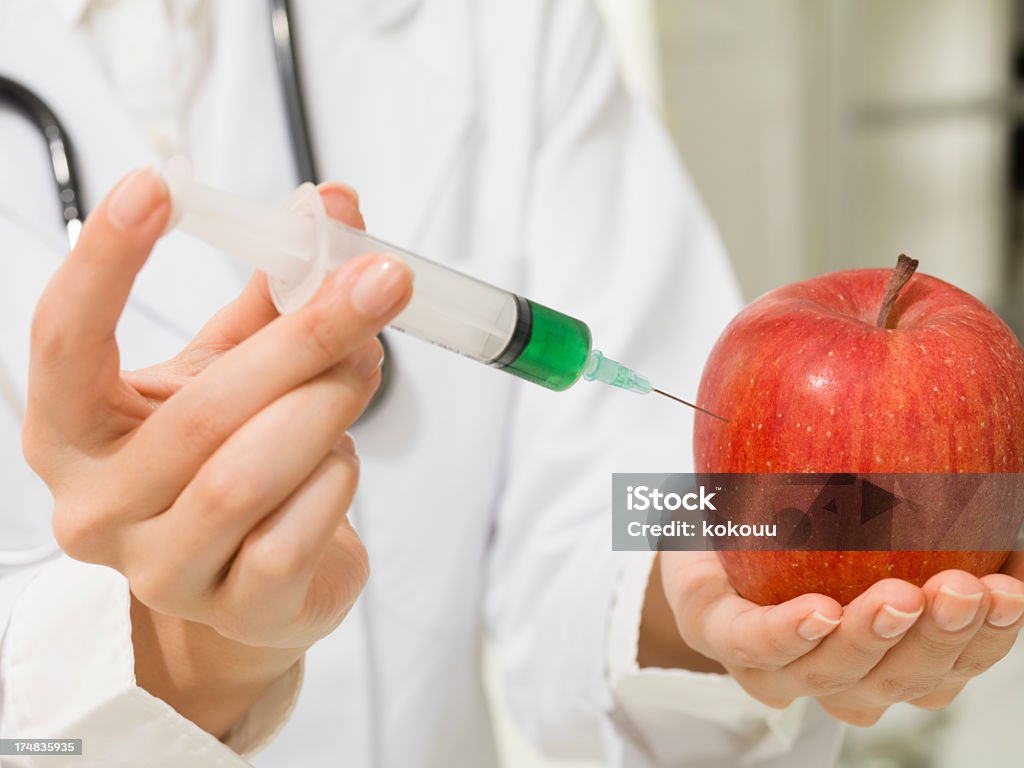 Female doctor who stabs an apple with injector Female doctor who stabs an apple with injector  Adult Stock Photo