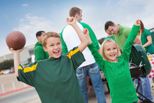 Excited children cheering at tailgate party during college football game.
