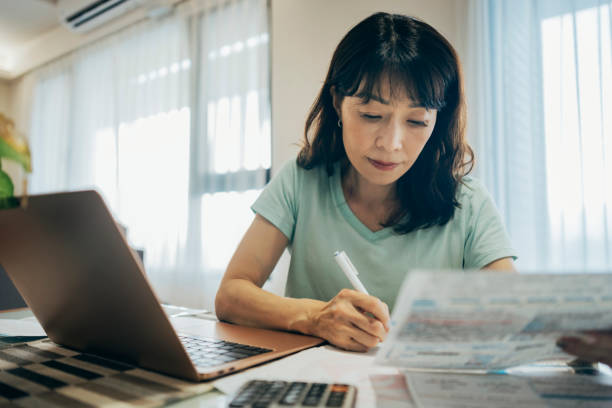 istock woman thinking about high prices while looking at utilities, gas, electricity, rental charges, water bill due to inflation and crisis. Planning personal budget while sitting in kitchen. Weighing options on how to save money 1748382037