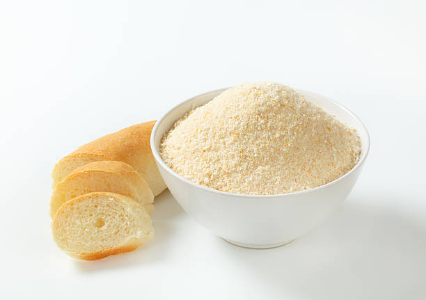 white ceramic bowl of fresh breadcrumbs and a sliced hard roll on a white background