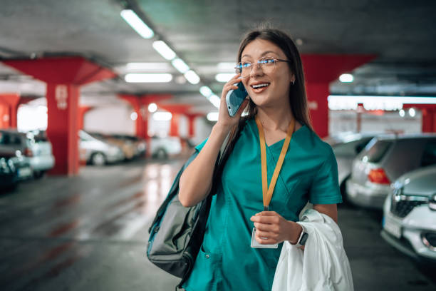 istock Young female nurse in scrubs cheerfully talking on a mobile phone, while on her way to work 1748386883