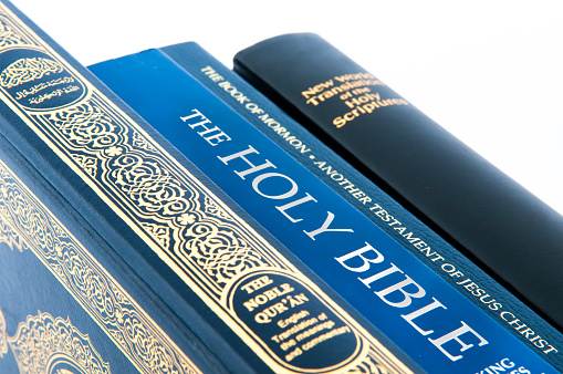 Stack of holy books - New World Translation of the Holy Scriptures, Book of Mormon, Holy Bible and the Qu'ran (Arabic inscription \