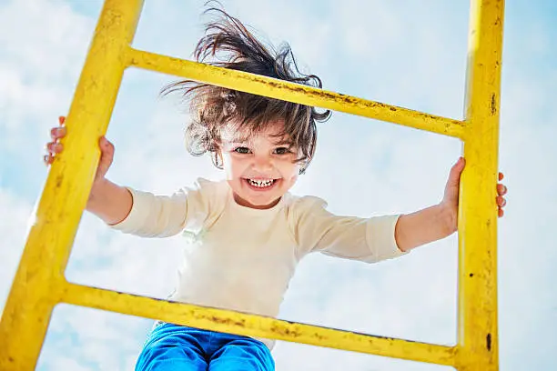 Cute little smiling while she is climbing on the playground and having fun. Portrait of adorable female child while playing on playground in a children park. See more images like this in: