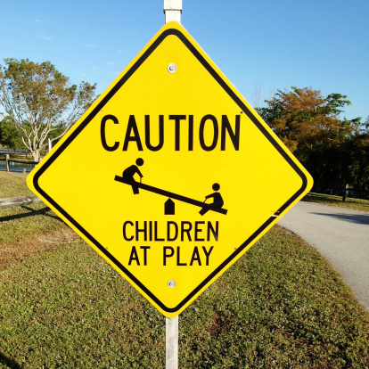 A yellow caution street sign warns of children at play in the area. Sign is near a road in a park.Mobilestock image taken with an Iphone5 mobile device.