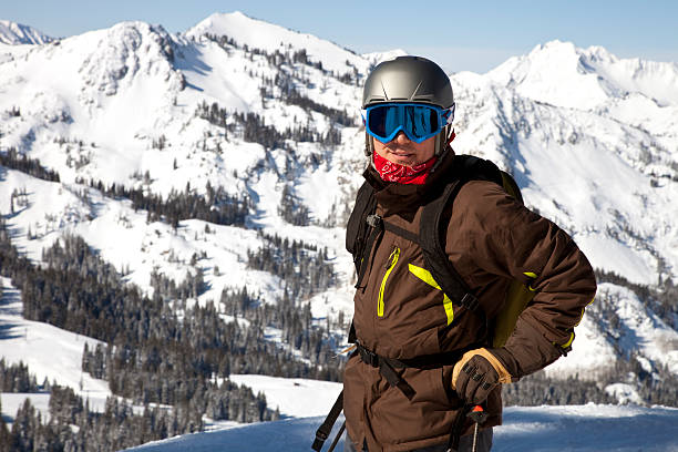 Snow Skier in snow suit and goggles posing looking at camera at top of mountain in Utah, snow filled mountains in background. Image shot with, Canon 5D Mark2, 100 ISO, 24-115mm lens 