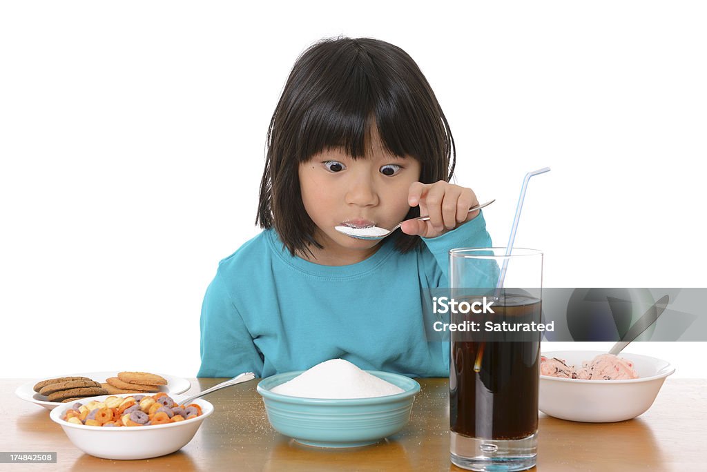 Excess Sugar: Child Eating Too Much Sweet Food A young girl stares cross-eyed at a spoonful of sugar she's eating while surrounded by sugary foods.White background. Eating Stock Photo