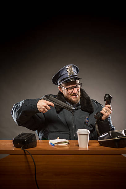 policeman señalando su pistola de teléfono - desk police police station humor fotografías e imágenes de stock