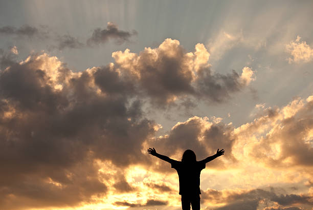 Happy Child A happy child raising his arms to the sky at sunset. Horizontal colour image. Copyspace. Worship concept. Silhouette. Natural God beams in the sky. religion sunbeam one person children only stock pictures, royalty-free photos & images