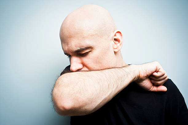 A man coughing into his arm on a blue background stock photo