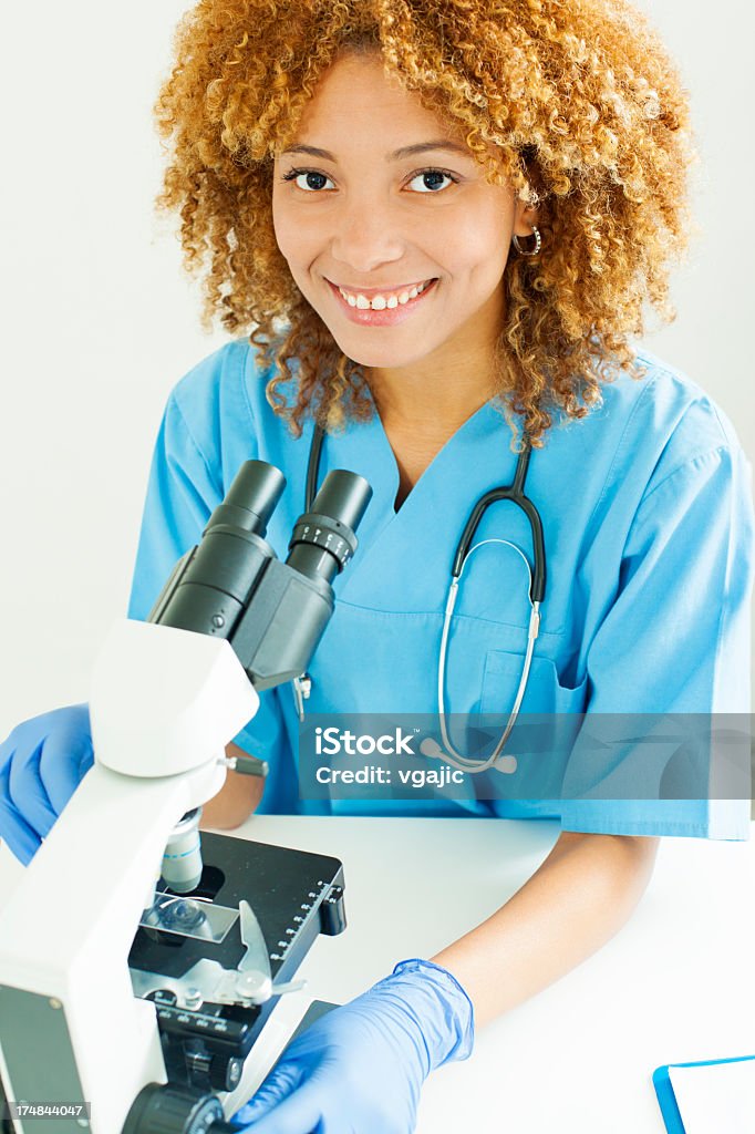 Dottore sorridente e lavorando per microscopio. - Foto stock royalty-free di Adulto