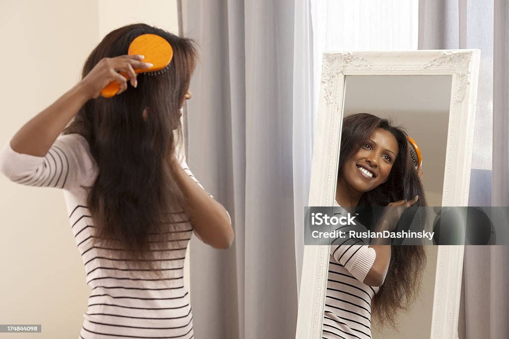 Woman brushing her hair. Smiling young woman brushing long straight hair  looking into beautiful vintage mirror. 25-29 Years Stock Photo