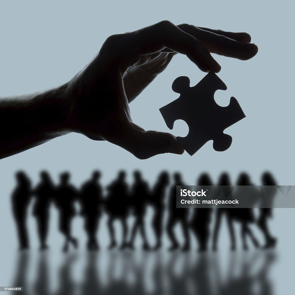 Team strategy Hand holding jigsaw puzzle piece over group of people Back Lit Stock Photo