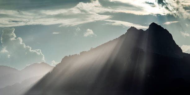 voluminous grazing light beams over the crest of the hahnenkamm mountains at sunset after a thunderstorm - hahnenkamm imagens e fotografias de stock