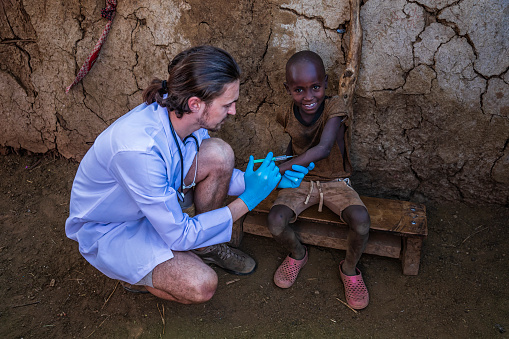 Male doctor is doing an injection to little African boy in small Masai village, Southern Kenya. Maasai tribe inhabiting southern Kenya and northern Tanzania, and they are related to the Samburu.