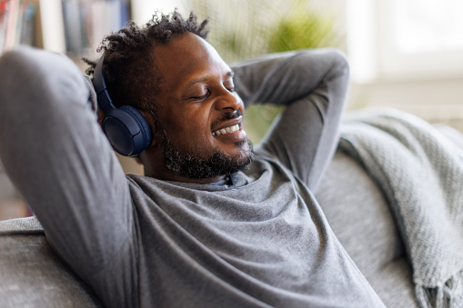 Smiling man enjoying music over headphones while relaxing on the sofa at home