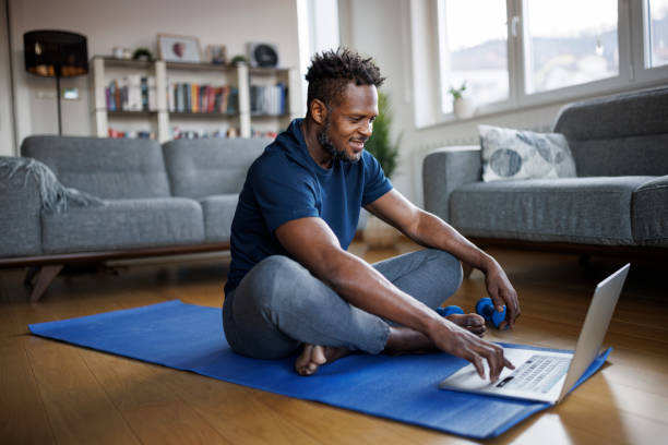 Smiling man scrolling on his computer laptop before doing daily workout at home stock photo