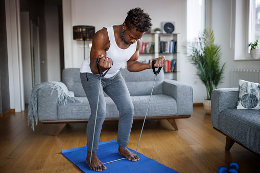 Young athletic man training with stretching band at home