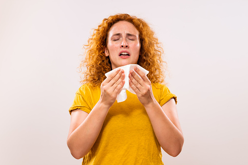 Ginger woman is having flu and she is sneezing.