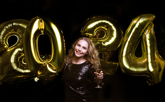 Happy gorgeous girl in stylish sexy party dress holding gold 2024 balloons, having fun at New Year's Eve Party