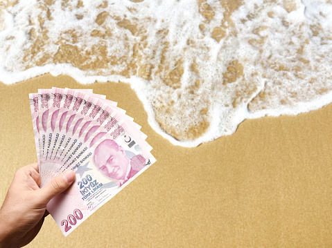 Vacations holiday budget concept. Hand holding Turkish lira banknotes with beach background. Turkish paper currency with sea and sand background