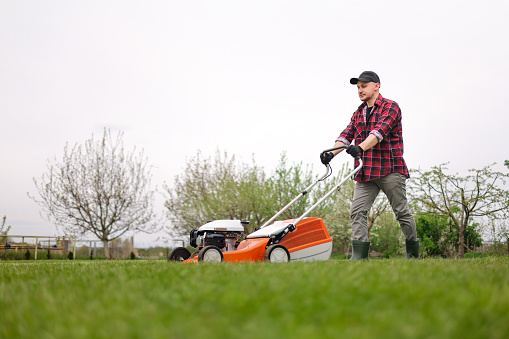 Cropped picture of a man cutting grass with a mower in a public place.