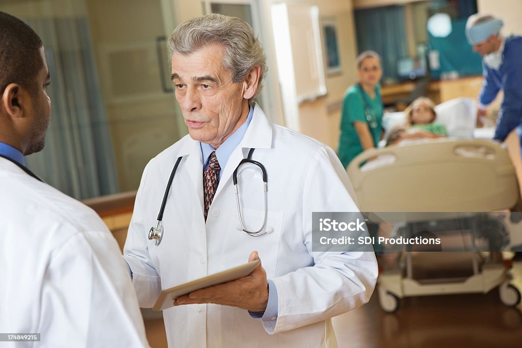 Médico sênior instruindo colega no corredor do hospital - Foto de stock de Acidentes e desastres royalty-free