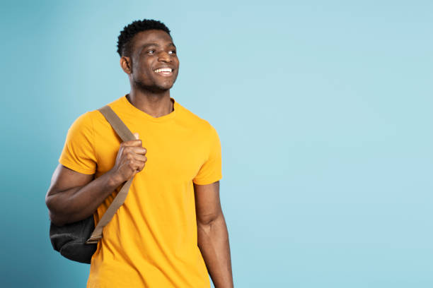 Smiling African American student holding backpack isolated on blue background, education concept