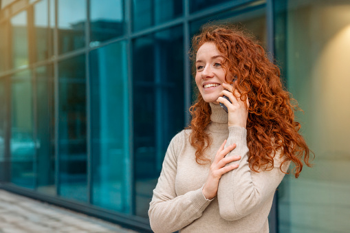 Portrait of beautiful happy young woman graduate with curly red hair talking on the mobile and excited  about news regarding her job application