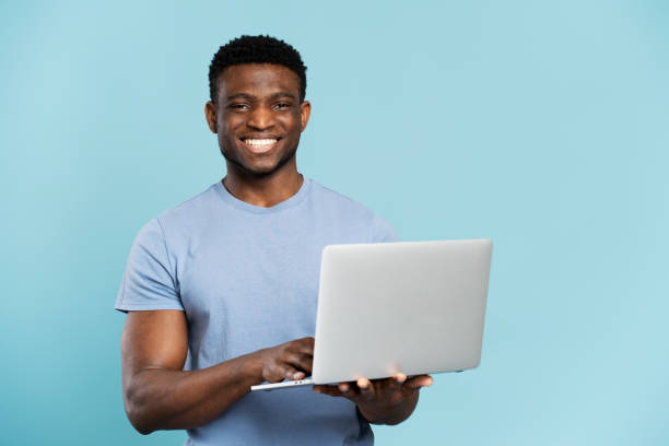 istock Portrait of handsome smiling African computer programmer holding laptop isolated on blue background 1748510121