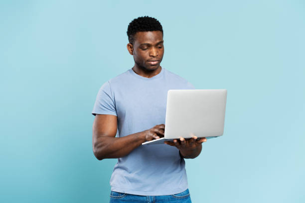 istock Serious nigerian man using laptop, on blue background, copy space. Young student preparing for exam 1748514080