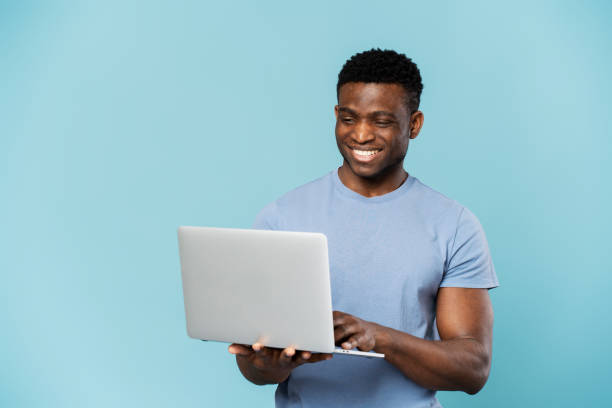 istock Smiling african american businessman using laptop isolated on blue background. Freelance concept 1748517281