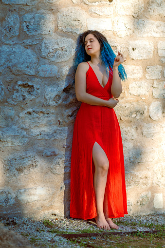 Attractive woman with blue hair and red dress poses in front of the Wall