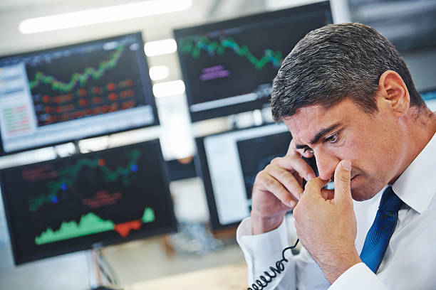 Our stocks are in trouble? Profile shot of a concerned businessman talking on the phone while sitting in front of monitors displaying financial information you are here stock pictures, royalty-free photos & images